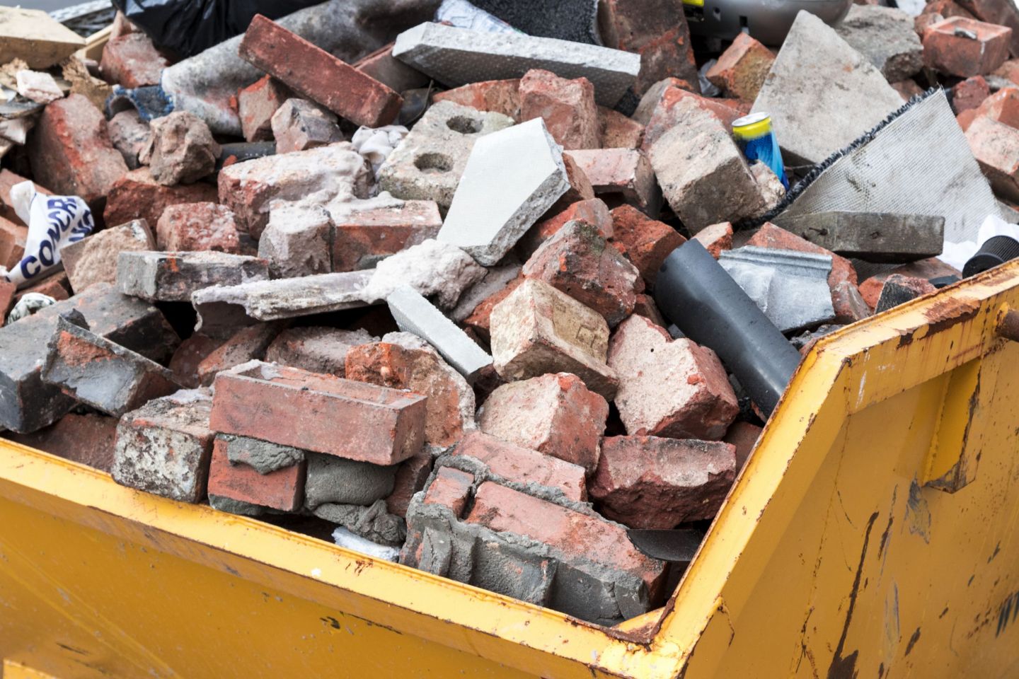 imagem de uma caçamba completamente cheia de tijolos e outros materiais descartados de uma obra civil 