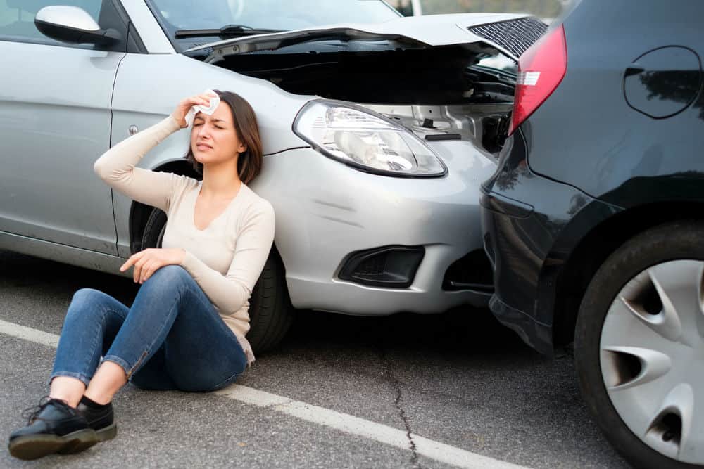 mulher encostada sob um carro durante uma batida de automóveis
